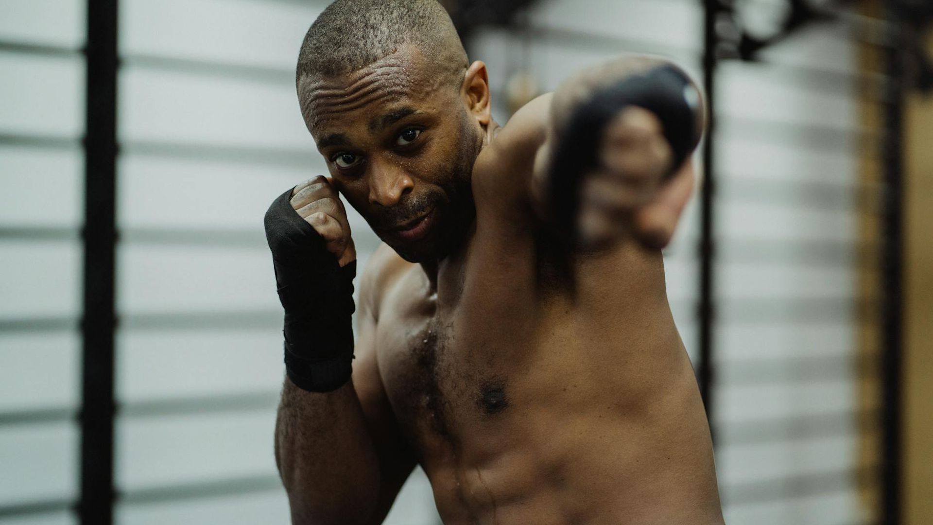 Man in a focused stance during a strength workout in a dark, minimalist setting.